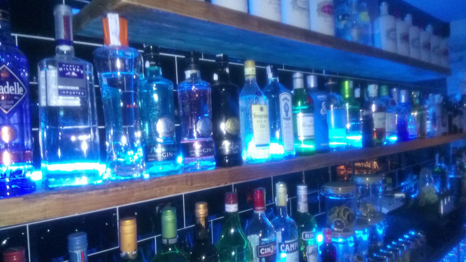 Estantería de la barra con botellas de ginebra iluminadas en azul