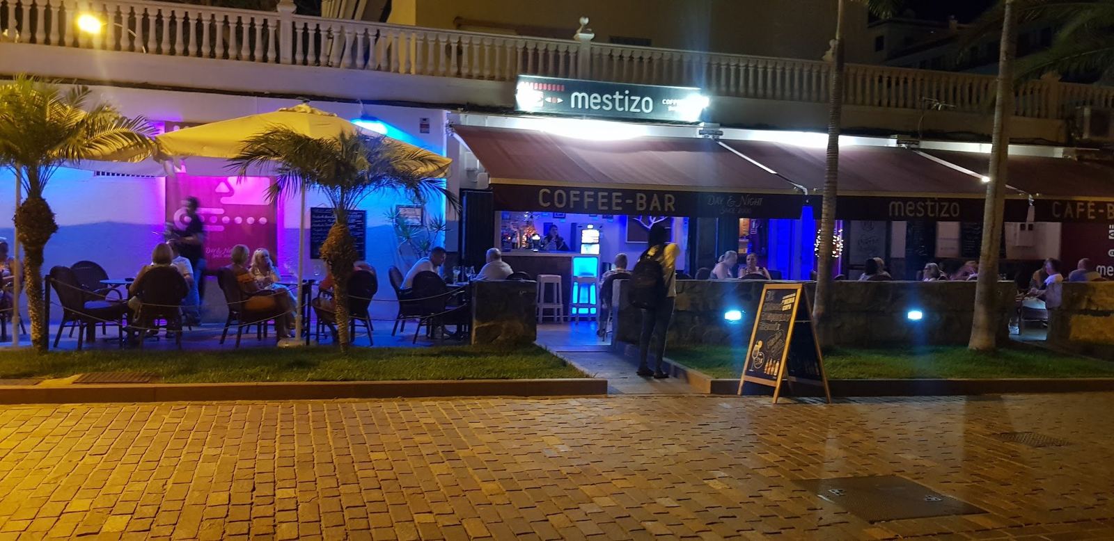 Fachada y terraza de Mestizo Café Bar de noche, con luz azul