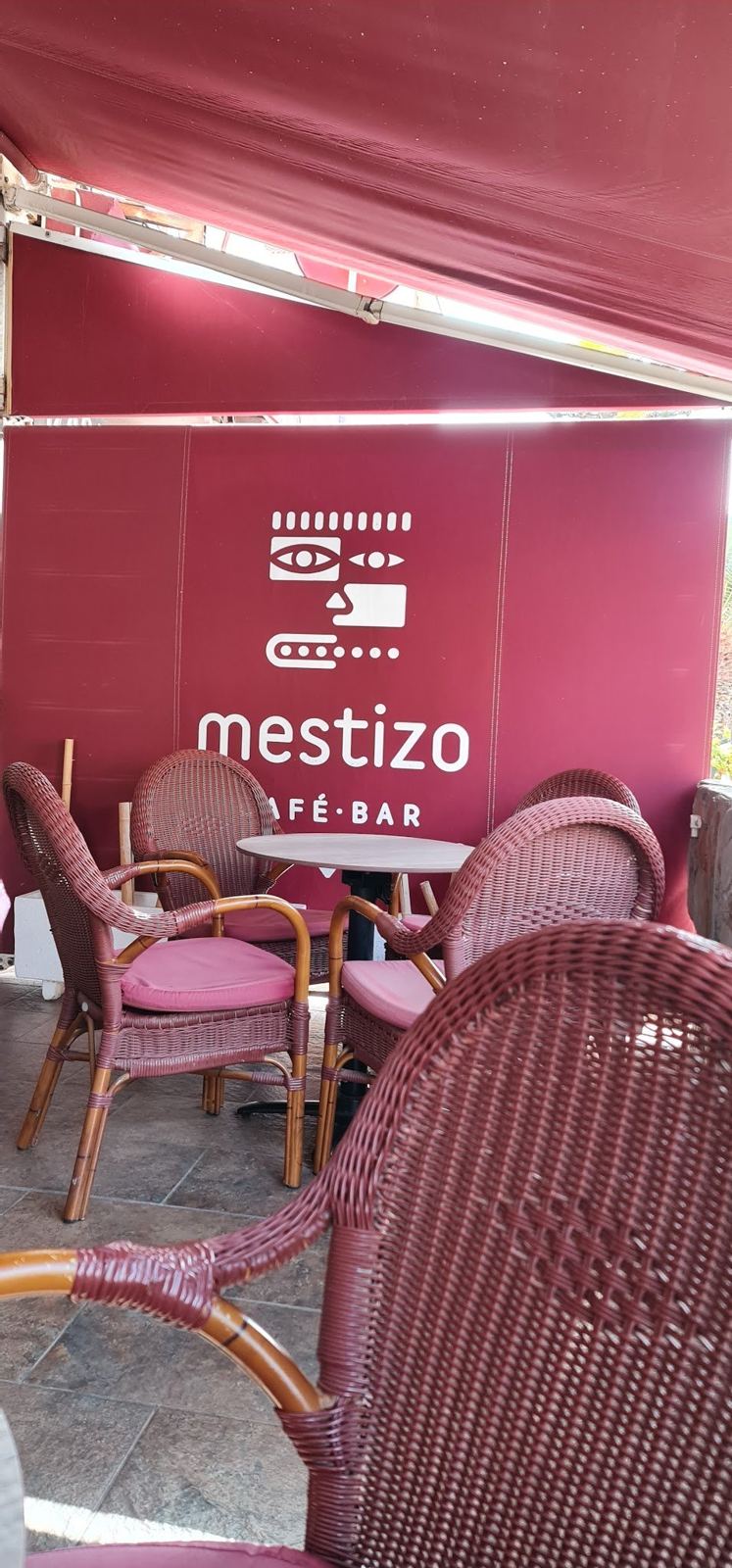 Terraza con sillones rojos y el logotipo de Mestizo en la lona